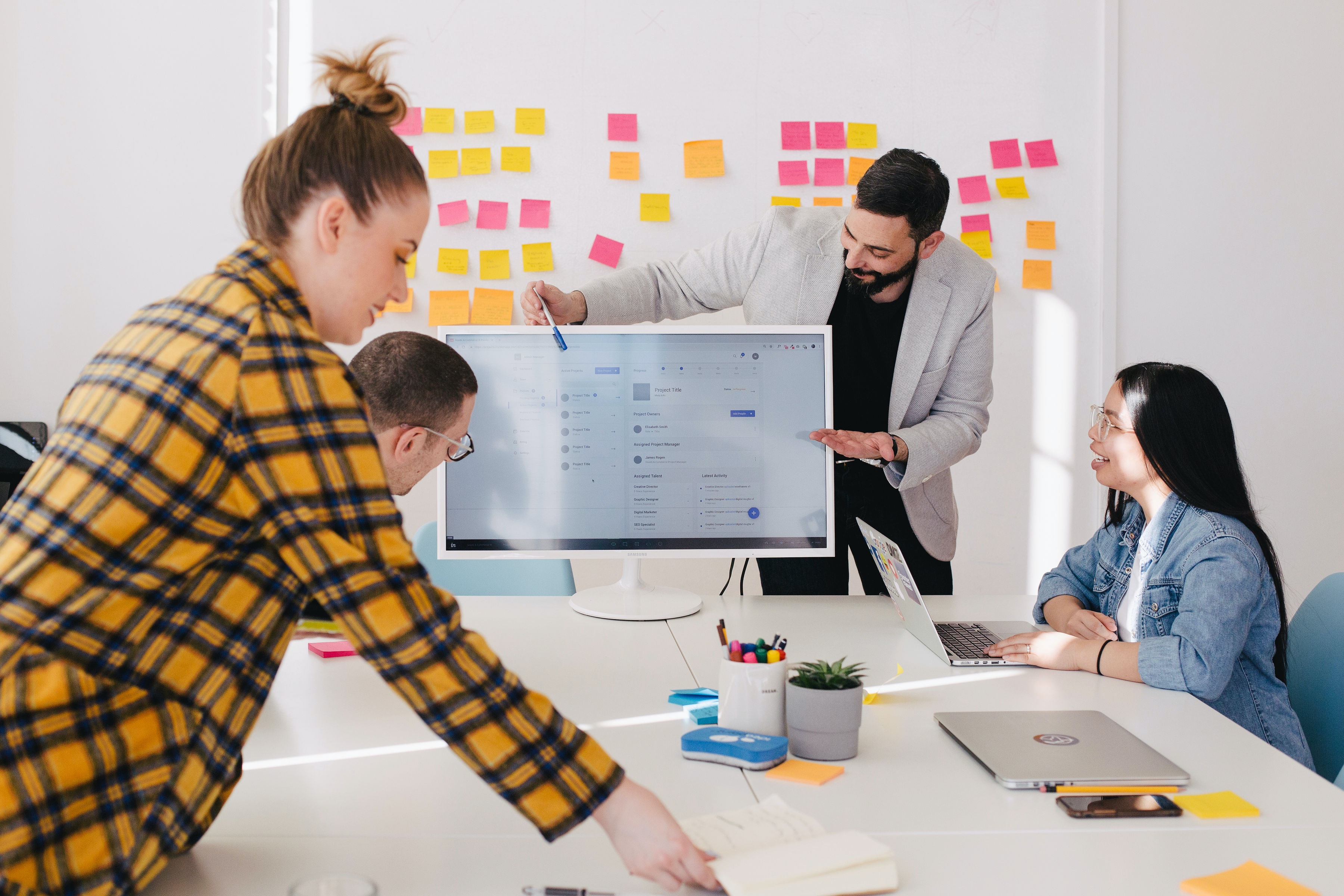 A team gathered around a screen in front of a wall of sticky notes
