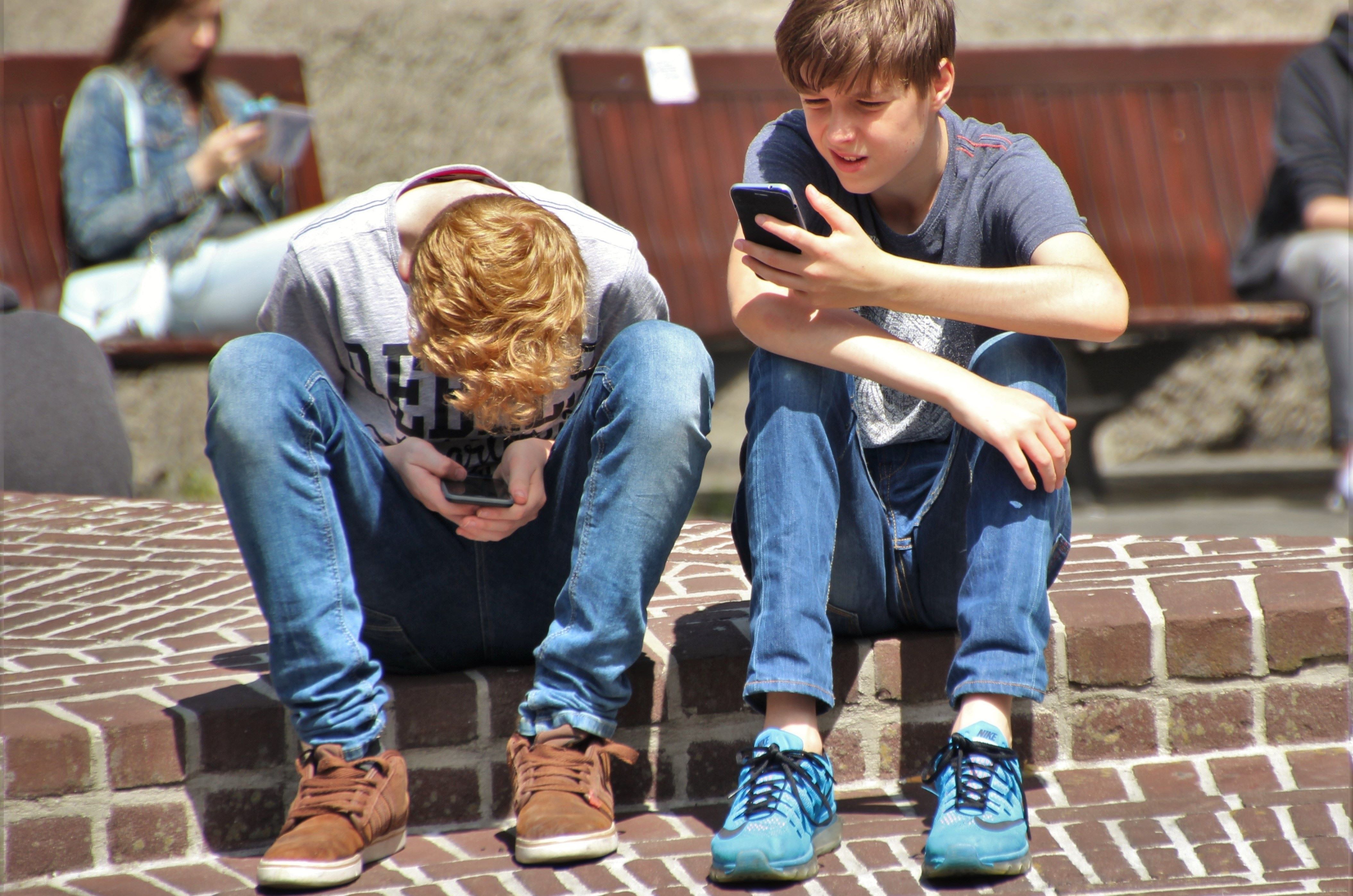 Two teenagers sitting on steps, looking at their phones