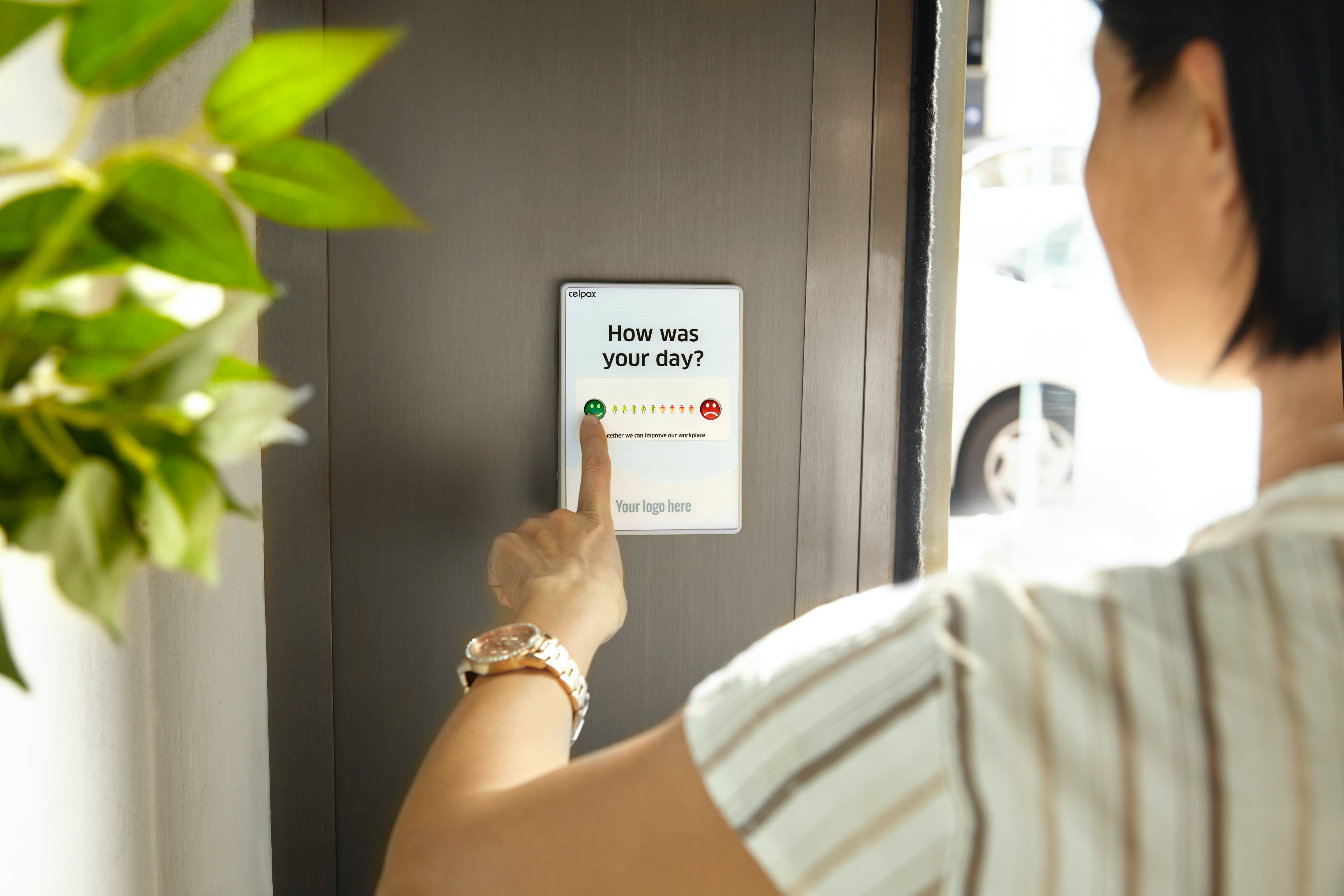 A person tapping a «How was your day?» rating screen on a wall